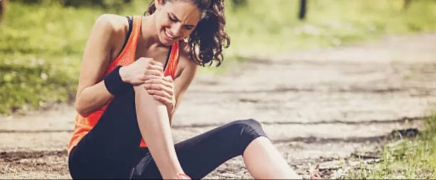 Runner sitting on a path holding their injured knee in pain
